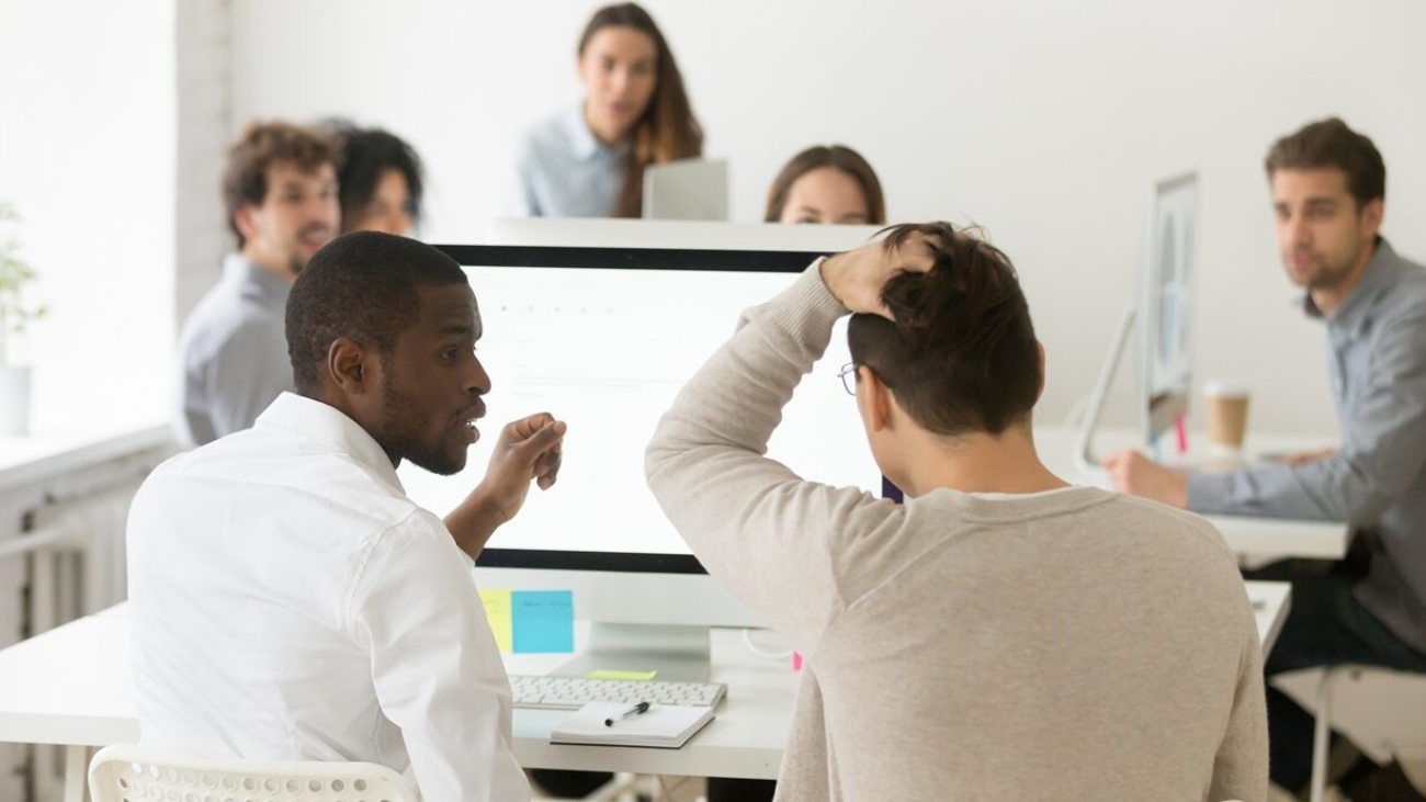 Rear view of stressed businessman suddenly realized problem mistake using pc with colleague in office, diverse team looking at frustrated coworker shocked by bad news online or unexpected dismissal
