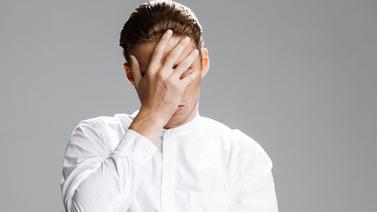 Picture of confused caucasian man hiding him face over white background.